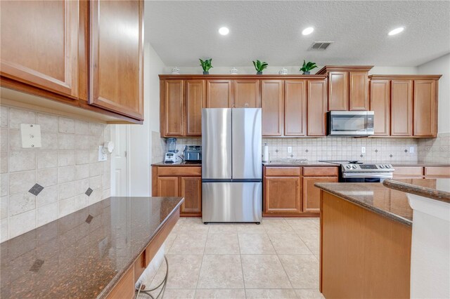 kitchen with visible vents, dark stone countertops, stainless steel appliances, light tile patterned floors, and decorative backsplash