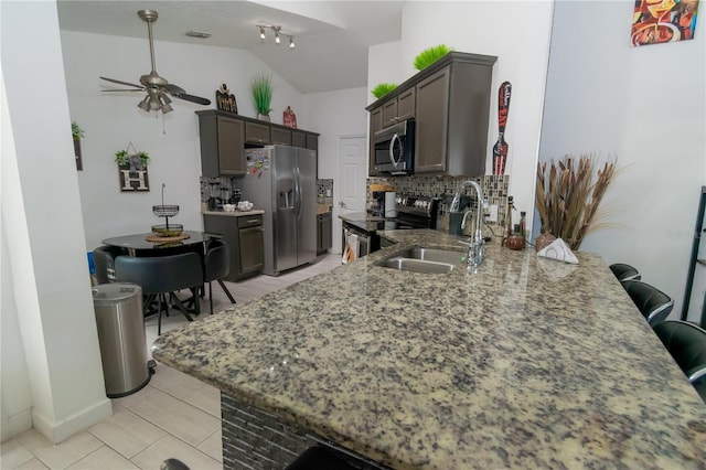 kitchen featuring a sink, light stone counters, a kitchen breakfast bar, stainless steel appliances, and decorative backsplash