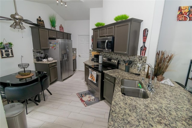 kitchen featuring light stone countertops, decorative backsplash, appliances with stainless steel finishes, a ceiling fan, and a sink