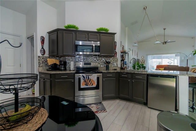 kitchen with backsplash, light stone countertops, a peninsula, stainless steel appliances, and a sink