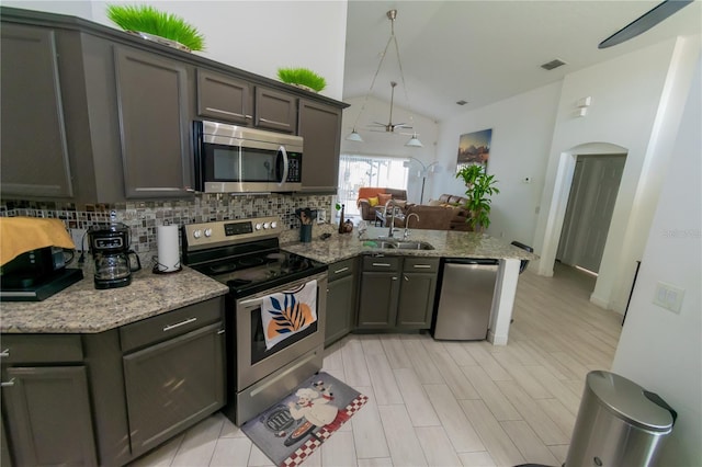 kitchen with vaulted ceiling, decorative backsplash, a peninsula, stainless steel appliances, and a sink