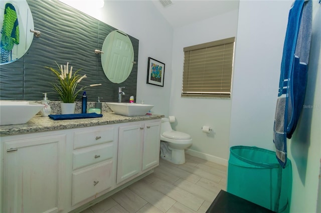 bathroom with double vanity, toilet, baseboards, and a sink