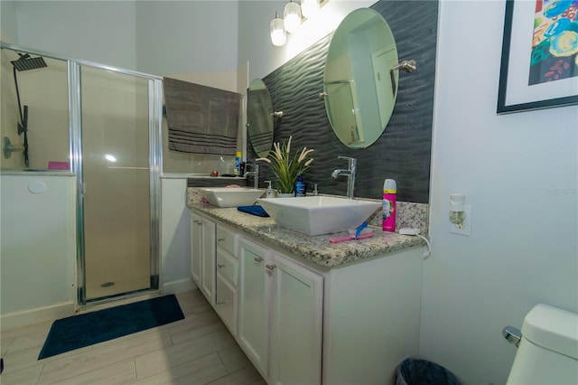 bathroom with a sink, toilet, a stall shower, and double vanity