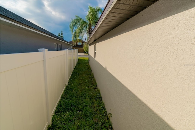 view of side of home with stucco siding, a lawn, and fence