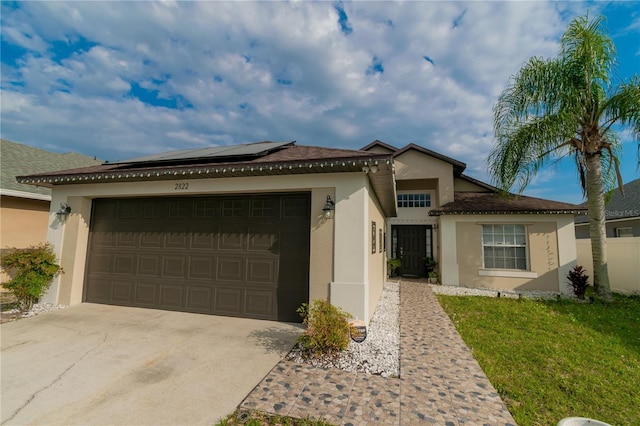 view of front of house with stucco siding, driveway, roof mounted solar panels, and an attached garage