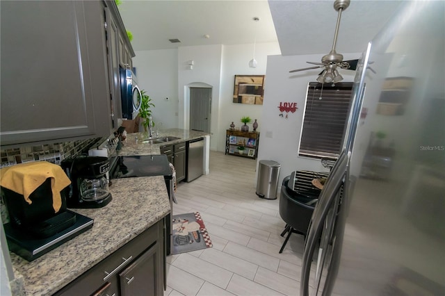 kitchen with light stone countertops, appliances with stainless steel finishes, arched walkways, a ceiling fan, and a sink