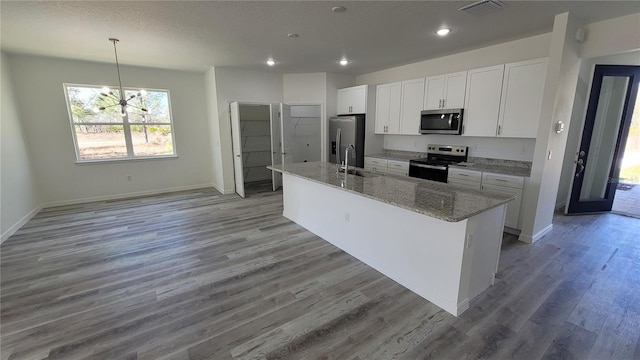 kitchen with visible vents, a center island with sink, light wood-style flooring, stainless steel appliances, and white cabinets