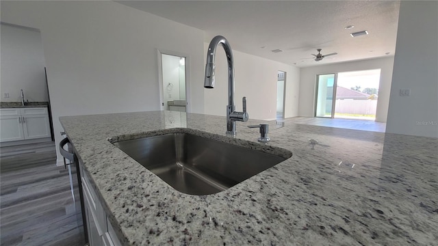 kitchen with visible vents, open floor plan, light stone counters, wood finished floors, and a sink