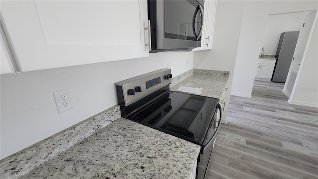 kitchen with white cabinetry, light wood-style floors, appliances with stainless steel finishes, baseboards, and light stone countertops