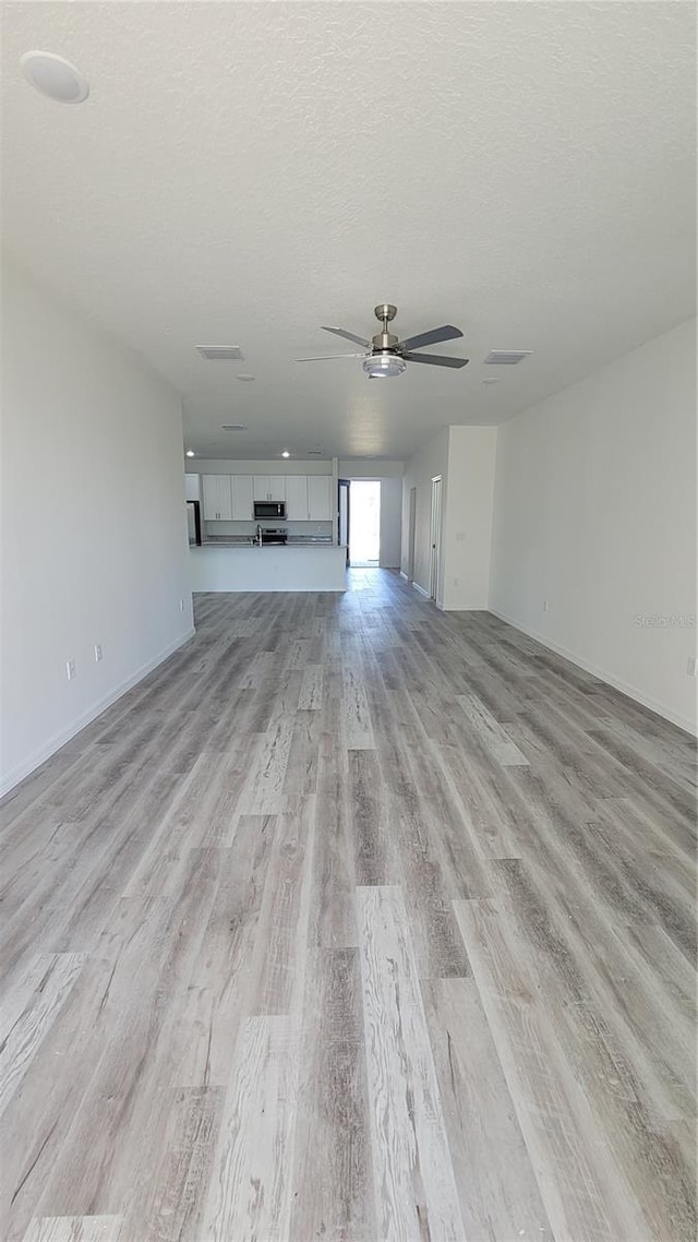 unfurnished living room featuring baseboards, a textured ceiling, light wood-type flooring, and ceiling fan