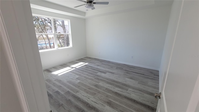 unfurnished room featuring a ceiling fan, a raised ceiling, baseboards, and wood finished floors