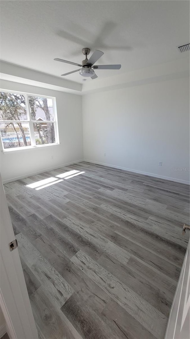 unfurnished room featuring a ceiling fan, wood finished floors, visible vents, and baseboards