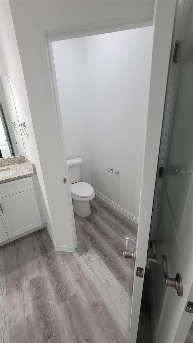 bathroom featuring baseboards, toilet, wood finished floors, and vanity