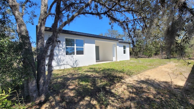 rear view of house featuring stucco siding and a lawn