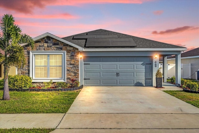 ranch-style home featuring a front lawn, stone siding, roof mounted solar panels, concrete driveway, and an attached garage