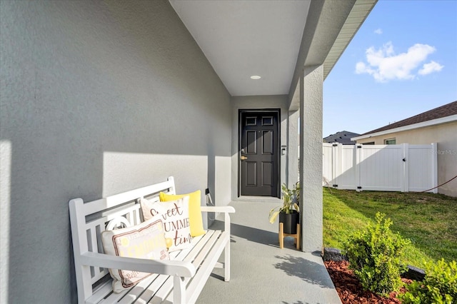 view of exterior entry with a gate, stucco siding, a lawn, and fence