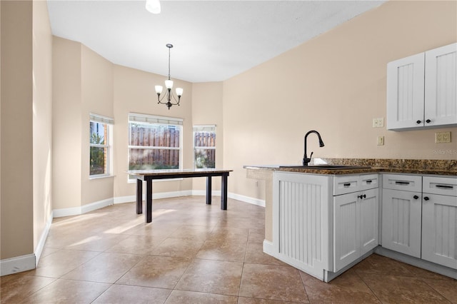 kitchen with dark countertops, a peninsula, an inviting chandelier, hanging light fixtures, and a sink