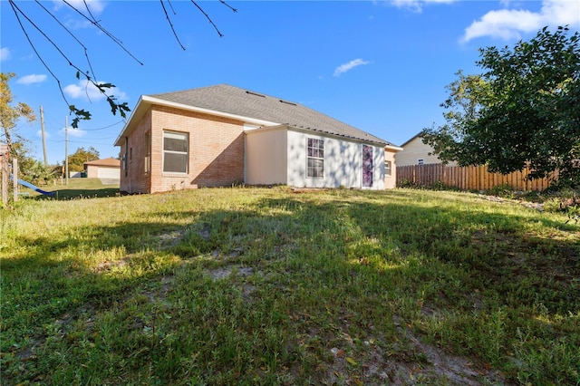 rear view of property featuring brick siding, a lawn, and fence