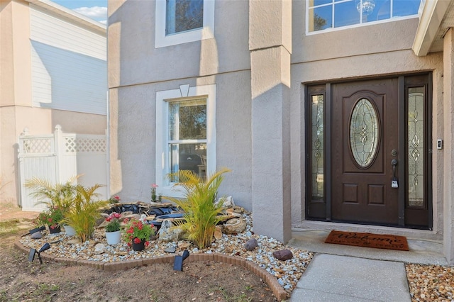 doorway to property featuring stucco siding and fence