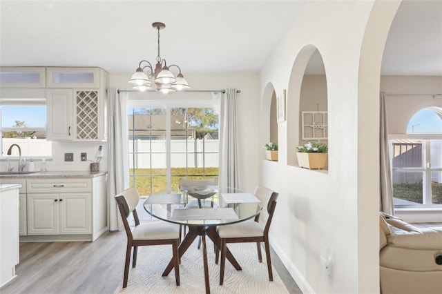 dining space featuring a chandelier, light wood-style flooring, arched walkways, and baseboards