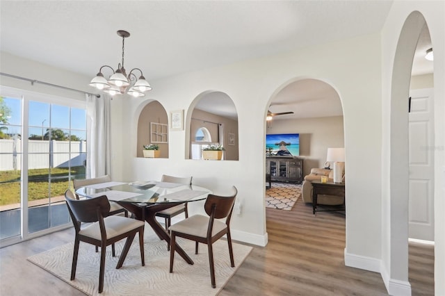 dining space featuring a notable chandelier, wood finished floors, baseboards, and arched walkways