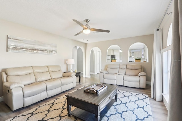 living area featuring light wood finished floors, arched walkways, baseboards, and ceiling fan