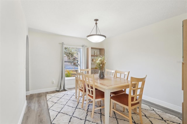 dining room with light wood-type flooring, baseboards, and arched walkways