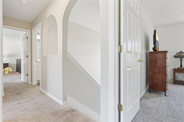 corridor featuring baseboards, carpet floors, and arched walkways