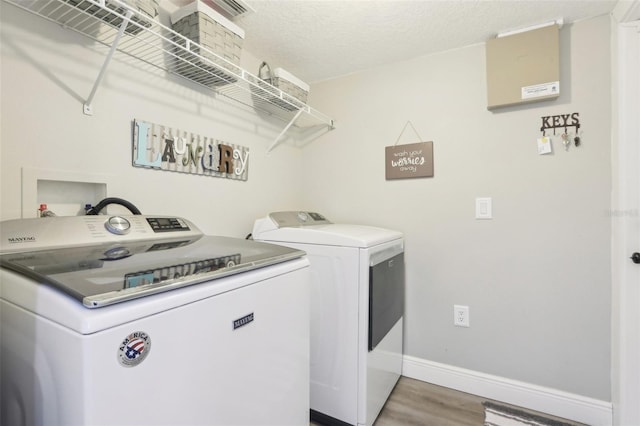 laundry room with baseboards, washing machine and clothes dryer, laundry area, light wood-style flooring, and a textured ceiling