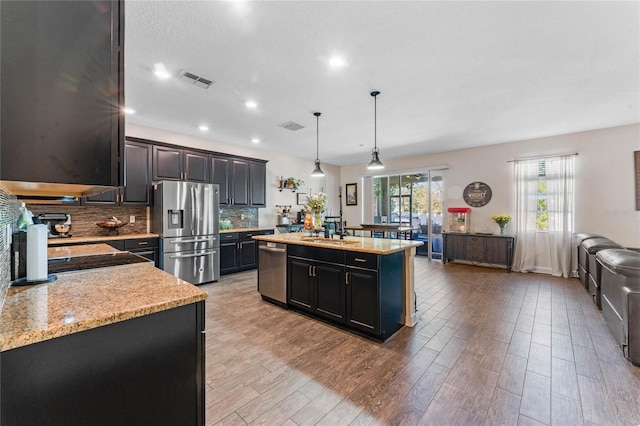 kitchen with visible vents, a center island with sink, a sink, stainless steel appliances, and backsplash