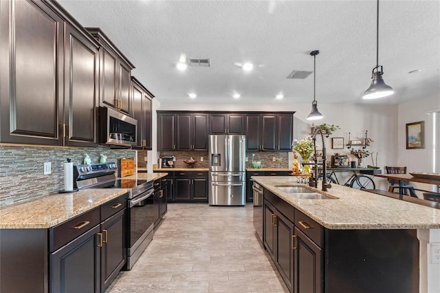 kitchen featuring a sink, visible vents, appliances with stainless steel finishes, and a center island with sink