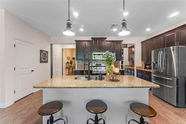 kitchen featuring hanging light fixtures, dark brown cabinetry, appliances with stainless steel finishes, a kitchen bar, and light wood-type flooring