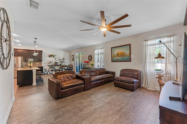 living area featuring visible vents, light wood-style flooring, baseboards, and ceiling fan