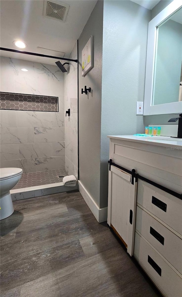 full bath featuring vanity, wood finished floors, visible vents, a tile shower, and toilet