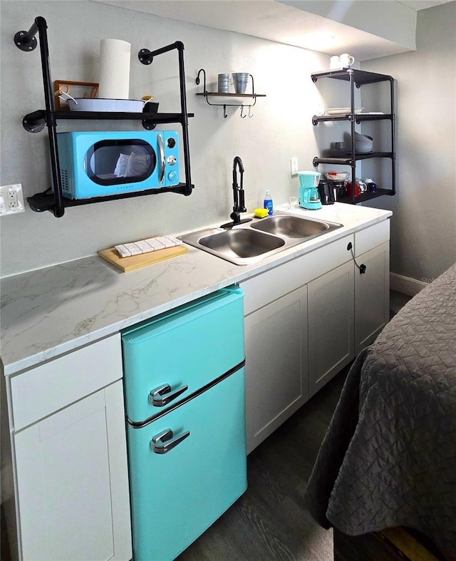 kitchen with a sink, open shelves, light stone countertops, and dark wood-style flooring