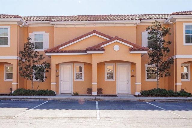 multi unit property featuring stucco siding, uncovered parking, and a tile roof