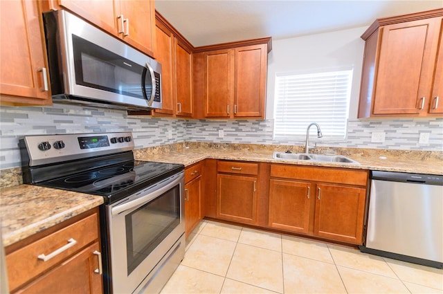 kitchen featuring light stone counters, light tile patterned flooring, a sink, stainless steel appliances, and brown cabinets