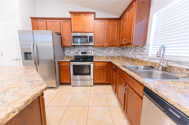 kitchen featuring lofted ceiling, light tile patterned flooring, a sink, appliances with stainless steel finishes, and brown cabinets