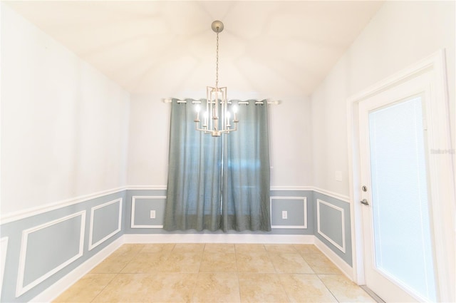 tiled empty room with an inviting chandelier, a decorative wall, and wainscoting