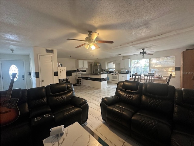 living area featuring a ceiling fan, visible vents, and a textured ceiling