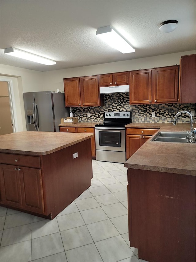 kitchen with a sink, under cabinet range hood, a textured ceiling, appliances with stainless steel finishes, and decorative backsplash