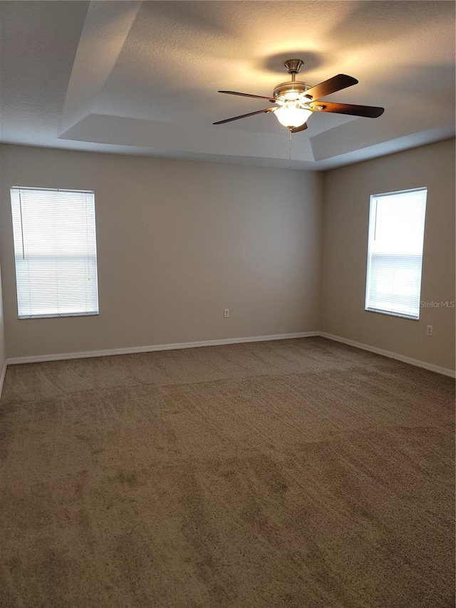 carpeted spare room featuring ceiling fan, baseboards, and a tray ceiling