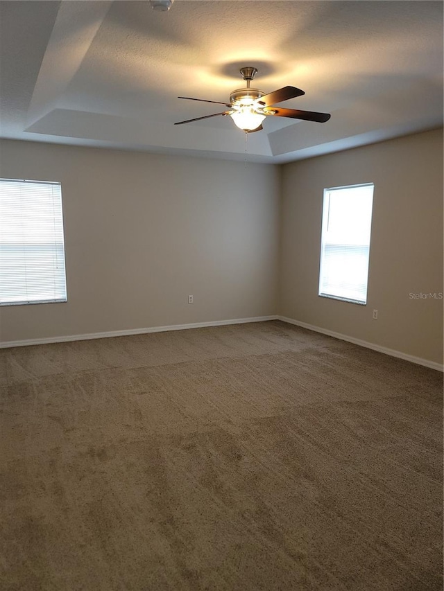 empty room with a tray ceiling, baseboards, carpet, and a ceiling fan