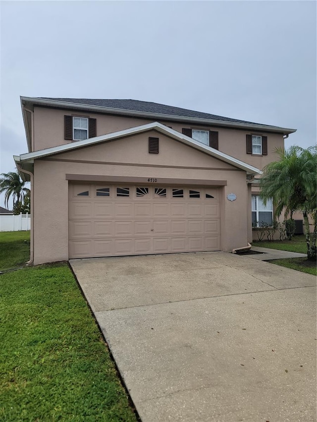 traditional-style house with concrete driveway, a garage, a front yard, and stucco siding