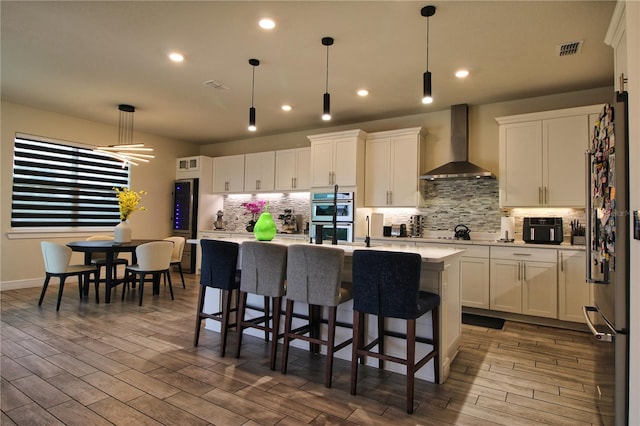 kitchen featuring visible vents, white cabinets, double oven, and wall chimney range hood