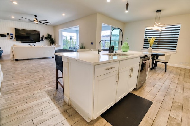 kitchen with white cabinetry, wood finish floors, a sink, stainless steel dishwasher, and open floor plan