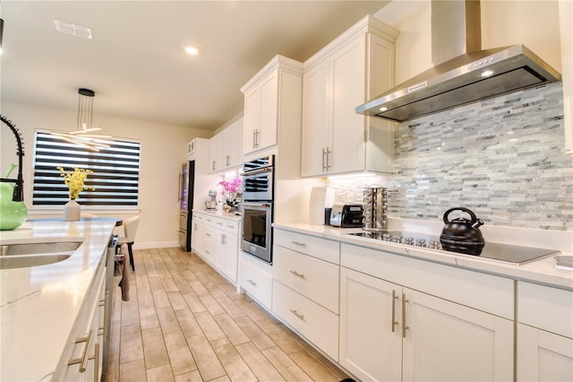 kitchen featuring backsplash, wall chimney exhaust hood, white cabinetry, and appliances with stainless steel finishes