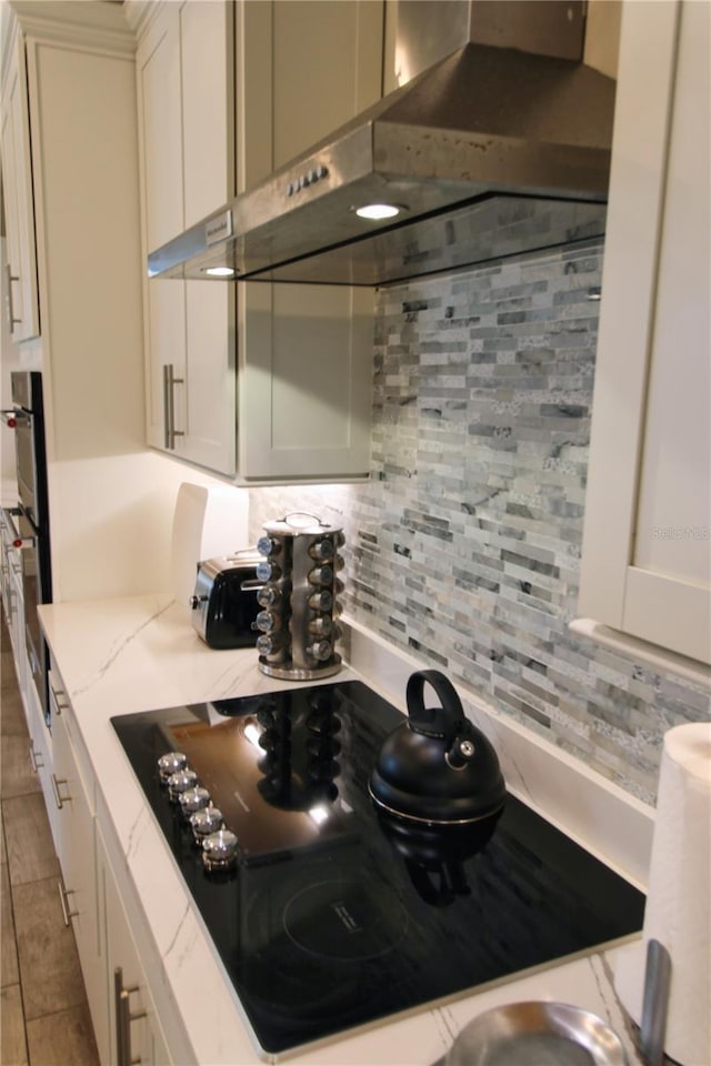 kitchen with range hood, light stone countertops, decorative backsplash, black appliances, and white cabinets