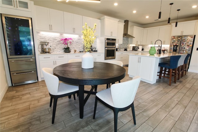 kitchen featuring wall chimney range hood, light countertops, fridge with ice dispenser, stainless steel double oven, and white cabinetry