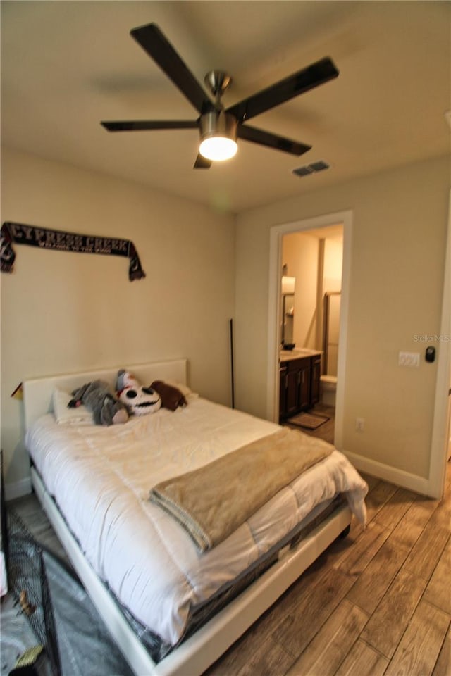 bedroom with visible vents, ensuite bath, wood finished floors, baseboards, and ceiling fan